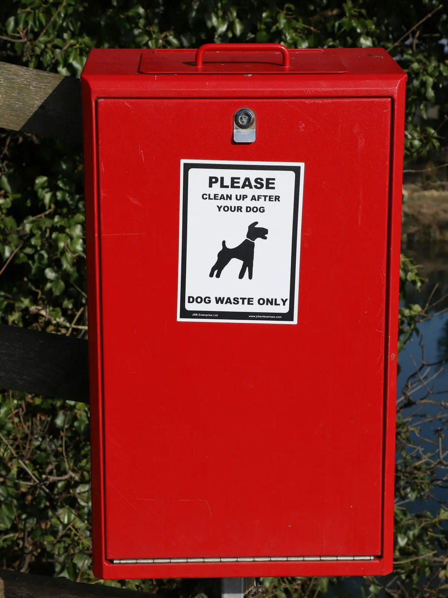 A red street-side box with a dog waste sign on a post